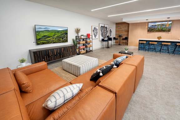 A living room with a brown leather couch and a television on the wall.