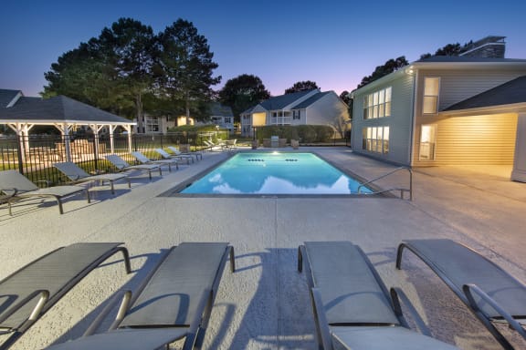a swimming pool with lounge chairs around it at night