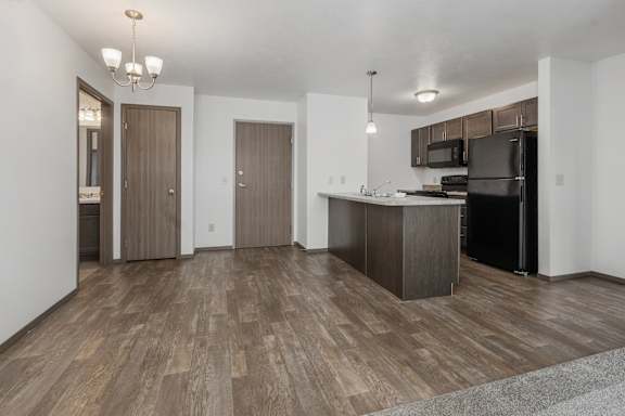 A kitchen with a black refrigerator and wooden floors.