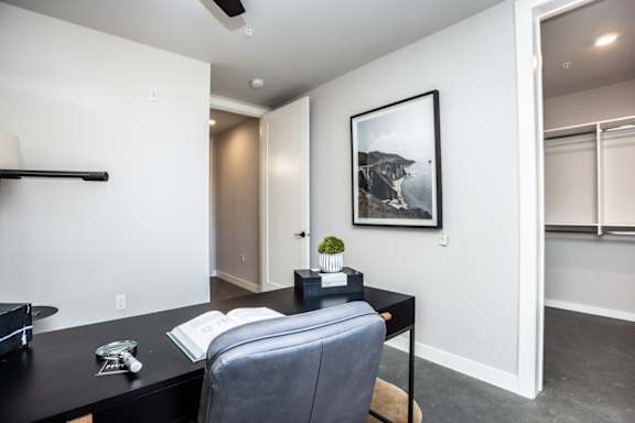 A black desk with a grey chair and a picture on the wall.