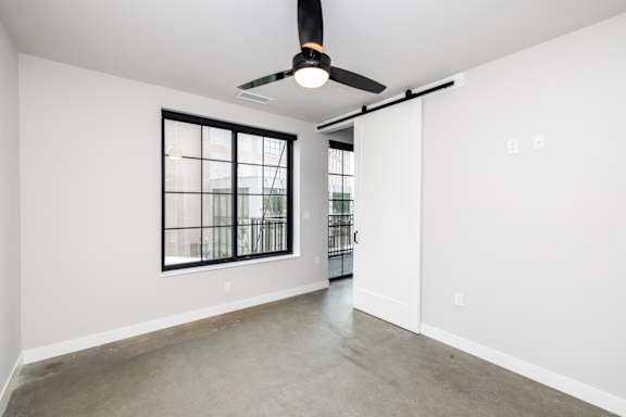 A room with a ceiling fan and a window with bars.