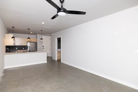 A spacious room with a ceiling fan and a kitchen area in the background.