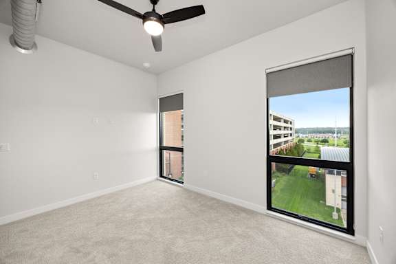 A room with a ceiling fan and a large window with a view of the outside.
