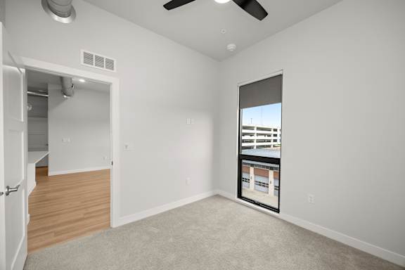 A room with a ceiling fan and a window showing a building outside.
