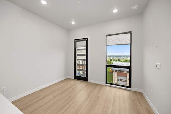 A room with a wooden floor and two windows showing the outside view.