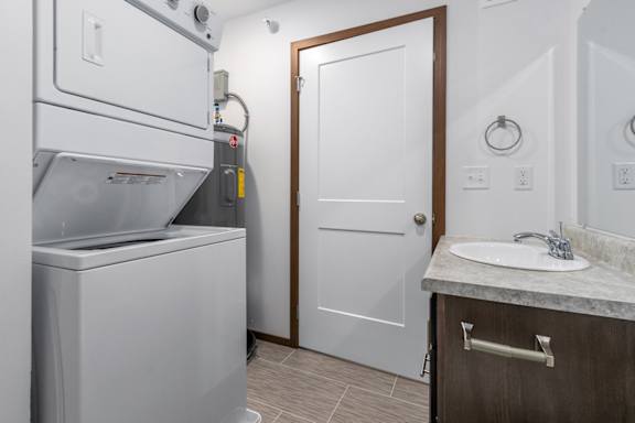 A white washing machine is in a small bathroom with a white door and a marble counter.