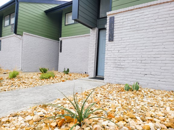 a sidewalk in front of a white brick house with green walls at Ivy Plains at Brooks Apartments, San Antonio , TX