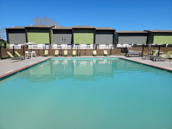 a swimming pool with chairs around it and a building in the background at Ivy Plains at Brooks Apartments, Texas, 78223