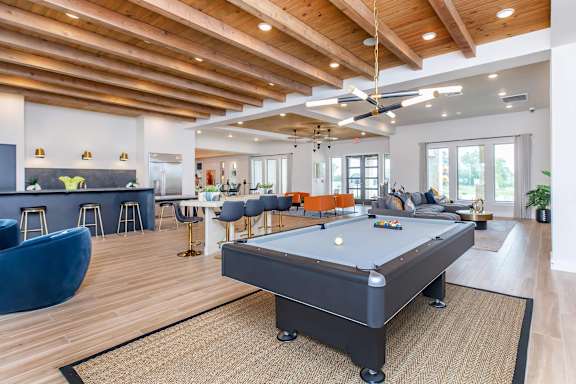 A billiard table is in the middle of a room with a bar and seating area.