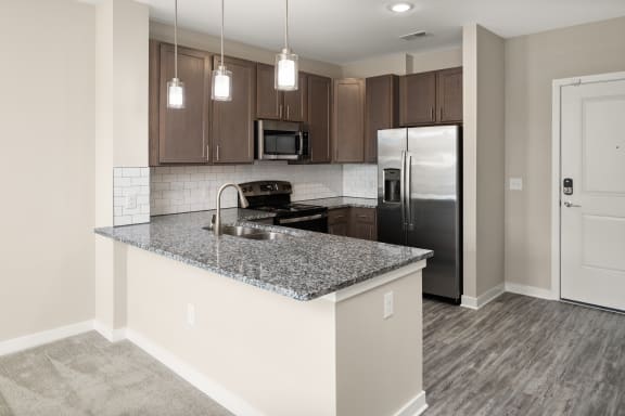 an empty kitchen with granite counter top and stainless steel refrigerator  at Abberly Liberty Crossing Apartment Homes, Charlotte, NC