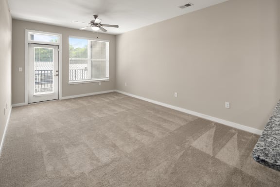 an empty living room with carpet and a door to a balcony at Abberly Liberty Crossing Apartment Homes, North Carolina