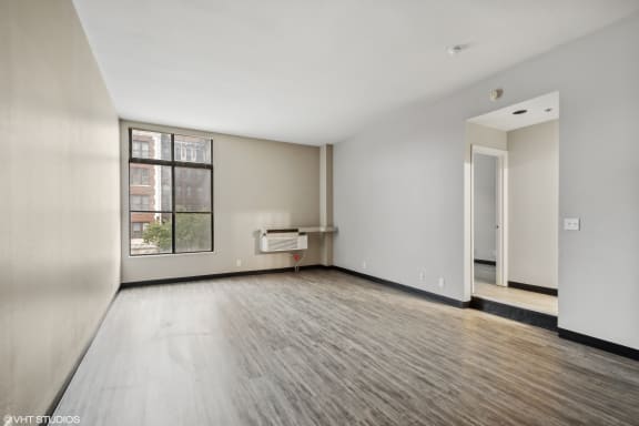 an empty living room with wood floors and a large window at Delmar Loop Apartments, St. Louis, MO