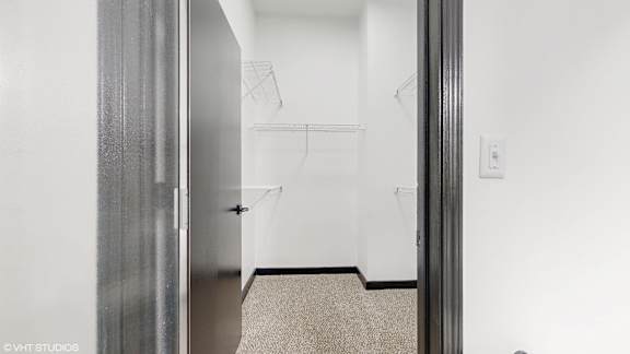 a walk in closet in a white room with a silver door