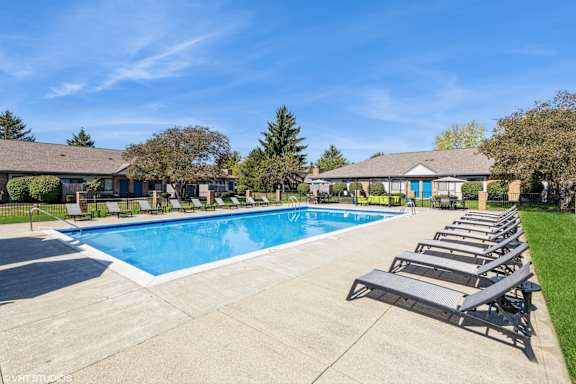 A large swimming pool surrounded by lounge chairs and houses in the background. at Karric Place of Dublin Apartments, Dublin, OH