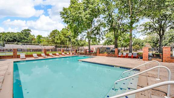 A large outdoor swimming pool surrounded by trees and lounge chairs.