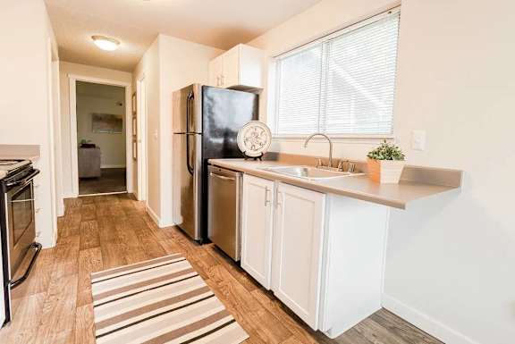 A kitchen with a black fridge, white cabinets, and a striped rug.