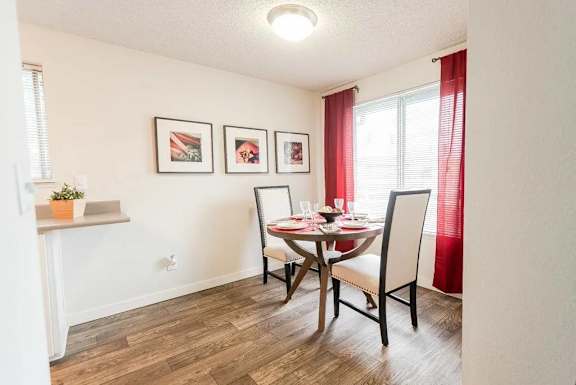 A dining room with a table set for two and a potted plant on the windowsill.