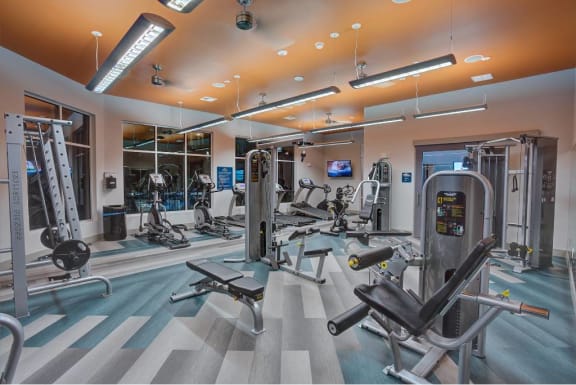 a gym with cardio equipment and mirrors in a building at The Grand at Stonecreek, San Marcos, TX