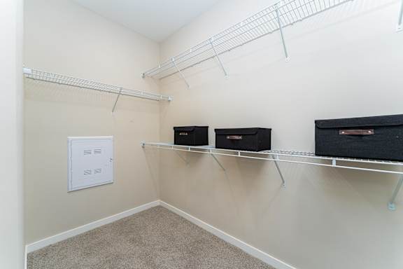 A room with a white ceiling, beige walls, and a carpeted floor with three black storage boxes on shelves.