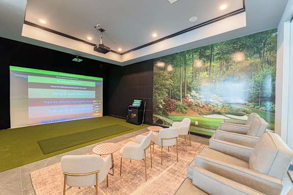 A golf simulator room with a screen and a green carpet.