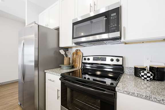 A modern kitchen with a stainless steel refrigerator, black oven, and white cabinets.