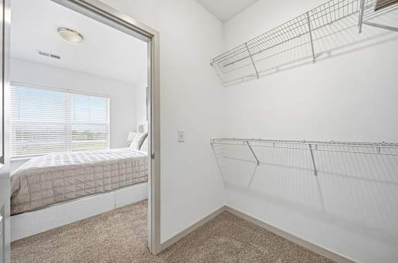 A white bedroom with a bed, a window with blinds, and a wall-mounted shelf.