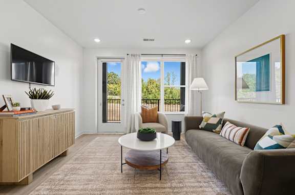 A living room with a grey couch, a white coffee table, and a flat screen TV mounted on the wall.