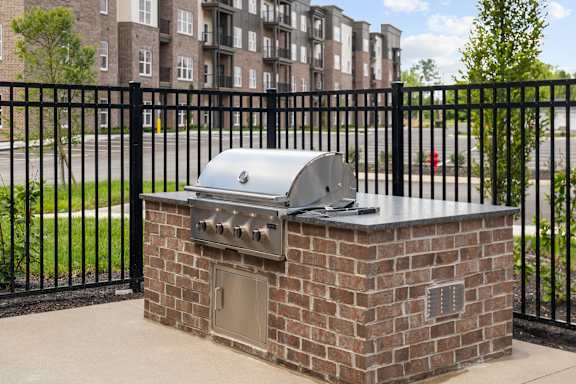 A brick barbecue grill is in front of a black fence.