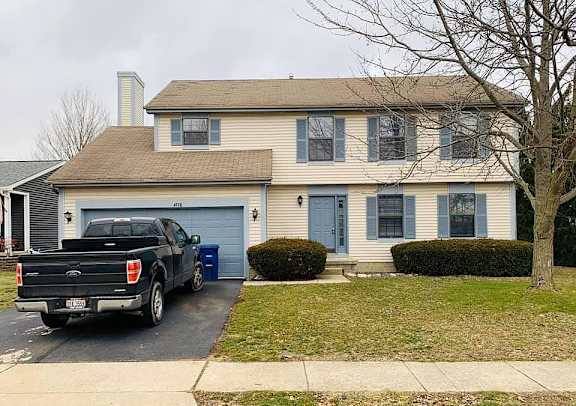 A black Ford truck is parked in front of a two-story house with a blue garage door.