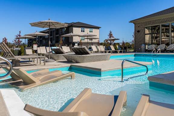 A pool with sun loungers and a building in the background.