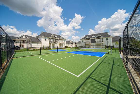 A tennis court surrounded by a fence and apartment buildings.