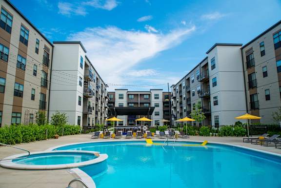 a swimming pool in front of an apartment building with yellow umbrellas