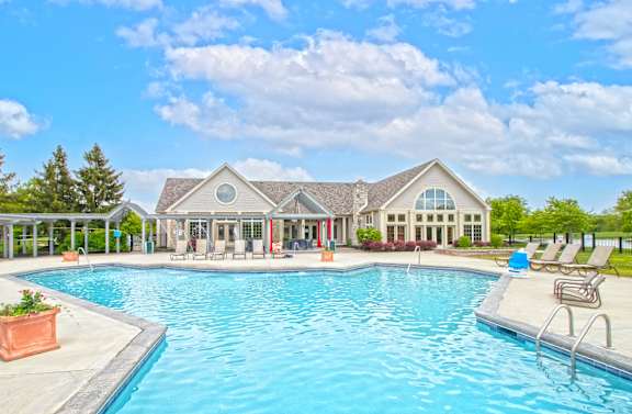 A large swimming pool in front of a house with a covered patio area.