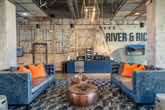 A blue couch with orange pillows sits in front of a wall with a map on it.