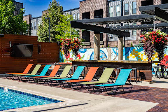 A pool with a row of colorful lounge chairs and a TV on a wooden stand.