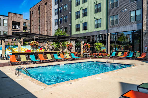 A pool surrounded by chairs and umbrellas in front of a building.