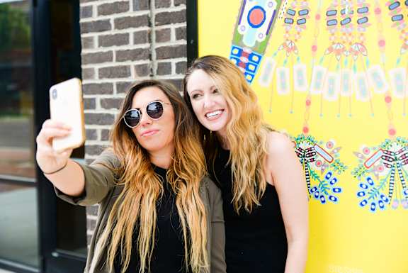 Two women taking a selfie in front of a colorful wall.