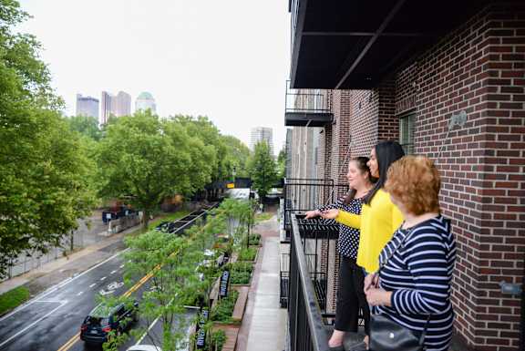 Two women are standing on a balcony overlooking a city street.