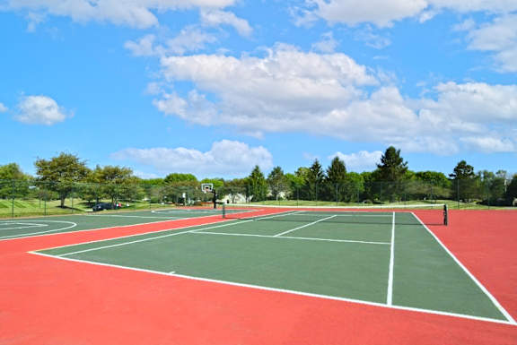 A red and green tennis court with a blue sky and clouds in the background.