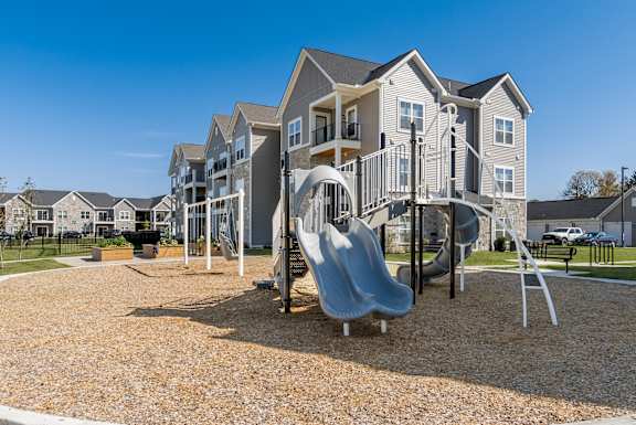A playground with a slide and swings in front of apartment buildings