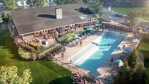 A large outdoor swimming pool surrounded by a grassy area and a building with a red roof.