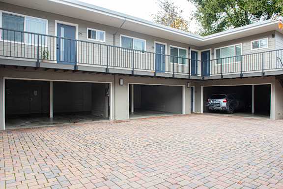 A car is parked in the garage of a two-story apartment building.