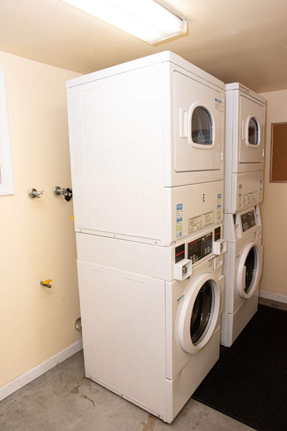 A stack of white front loading washing machines in a laundry room.