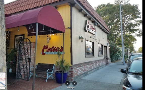 the outside of a restaurant with a yellow facade and a red umbrella