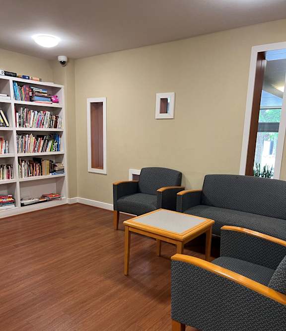 A room with a bookshelf, a chair, a couch, and a coffee table.