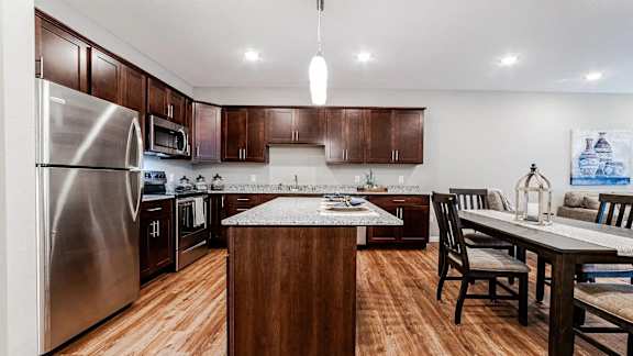a large kitchen with stainless steel appliances and a dining table. Circle Pines, MN Lexington Lofts