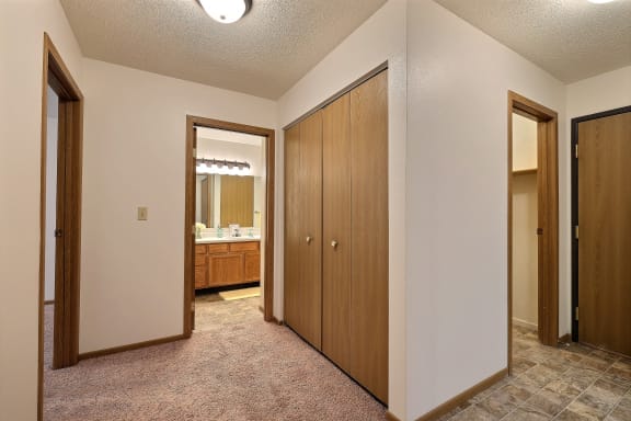 A hallway to the bathroom with a couple closets and the entry door. Fargo, ND Country Edge Apartments