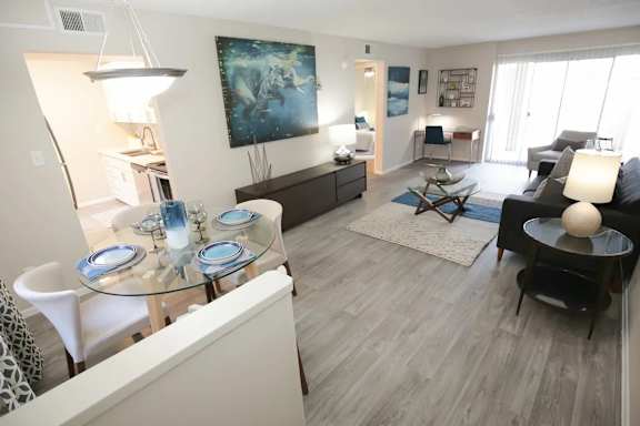 A modern living room with a glass dining table and a large painting on the wall.