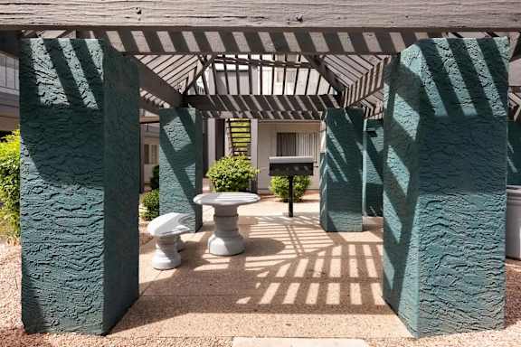 A patio with a table and chairs is framed by two green columns.