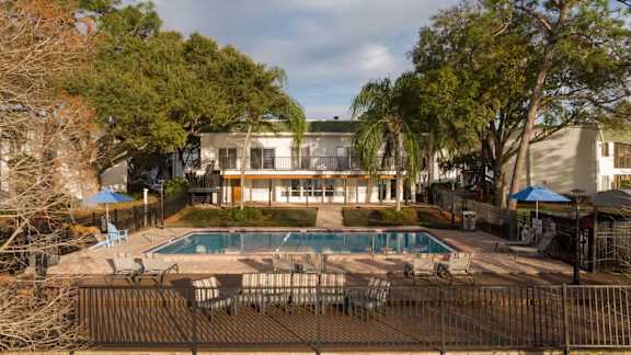 A pool surrounded by chairs and trees with a house in the background.